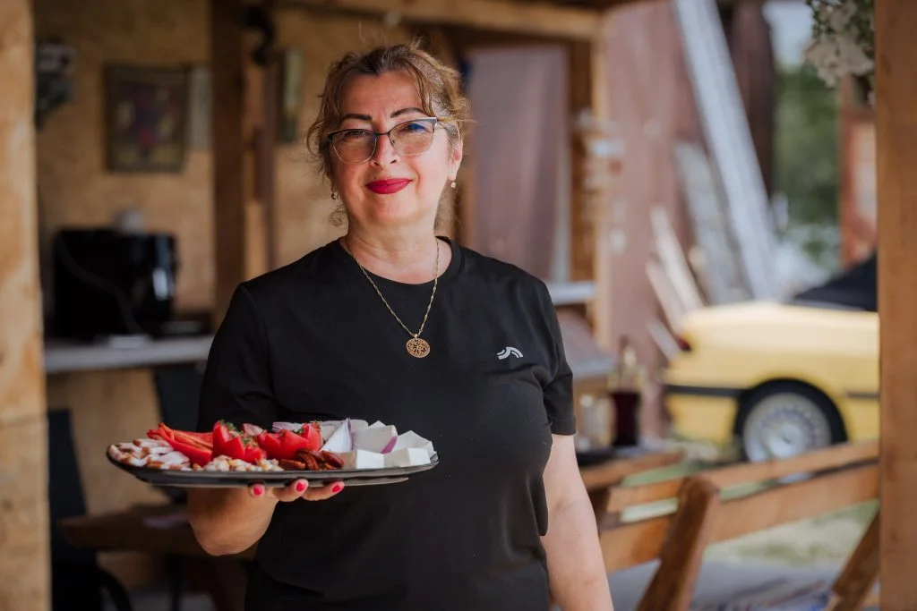 Gazda ține un platou cu brânzeturi, legume și mezeluri locale